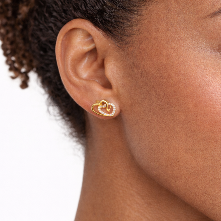 Close-up of a woman wearing gold heart-shaped earrings on a white background