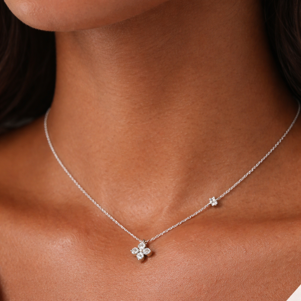 Silver necklace with a clover-shaped pendant on a person wearing a white top.